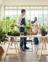 Gardener young Asian man woman two person family stand  smiling lookand helping organize small tree. Inside room  tree leaf green in calm work shop home plant . hobby job happy and care concept photo