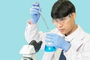 Asian man student scientist in reagent mixing laboratory In a science research laboratory with test tubes of various sizes. on the floor in  laboratory chemistry lab blue background. photo