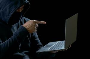 Hacker spy man one person in black hoodie sitting on a table looking computer laptop used login password attack security to circulate data digital in internet network system, night dark background. photo