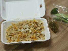 arroz frito con carne de cangrejo cubierto con huevo revuelto, comida tailandesa al estilo en una caja de papel blanco leída para comer, para llevar a casa foto