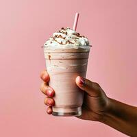 Closeup of female hand holding glass of chocolate milkshake with whipped cream on pink background photo