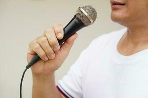 hombre sostiene y hablar o canta en micrófono. concepto, herramienta o dispositivo tecnología ese traduce sonido vibraciones en el aire dentro electrónico señales a altoparlante para entretenimiento o público discurso. foto