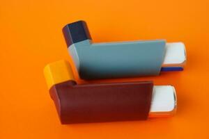 Asthma inhalers on orange background. Concept, Pharmaceutical products for treatment symptoms of asthma or COPD. Use under prescription. Health care device at home. photo
