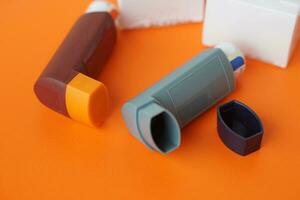 Asthma inhalers on orange background. Concept, Pharmaceutical products for treatment symptoms of asthma or COPD. Use under prescription. Health care device at home. photo