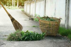 Closeup stick broom to sweep pile of grass beside the street and put in the basket. Concept, community service, get rid of grass and garbage beside street. photo