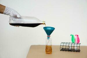 Close up hand holds bottle of soft drinks water to pour into the funnel bottle for doing science experiment.Concept, Science process about reaction of chemical substance. photo