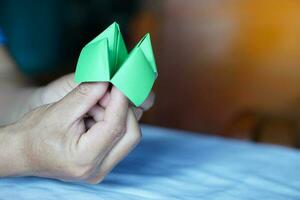 de cerca manos sostener verde origami papel fortuna cajero. concepto , vida oportunidad. papel juguete ese lata utilizar como creativo juego en verano acampar o salón de clases actividad para divertida. foto