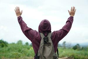 Back view of Asian man traveller raises two hands up to sky, feels free and happy with fresh air in nature. Concept, enjoy travelling. independent  adventure  lifestyle photo