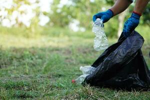 cerca arriba manos son cosecha el plastico botellas dentro negro basura bolso en el parque. concepto, mantener limpiar en público sitio para mejor ambiente. reciclar el plastico basura. foto