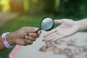 Closeup hand holds magnifying glass to inspect palm lines. Concept , palmistry, astrology. Foretelling, mystery, magic, fortune, fate. Prediction for future life , events.  Palmist predicting. photo