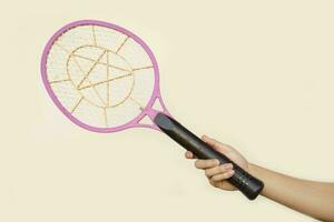 Closeup hand holds mosquito electric swatter racket. Concept, electric device to kill mosquitoes, insects, bugs by swatting to flying insects. photo