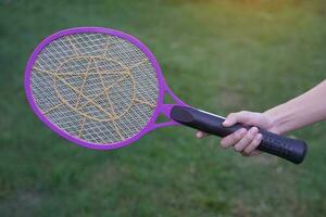 Closeup hand holds mosquito electric swatter racket. Concept, electric device to kill mosquitoes, insects, bugs by swatting to flying insects. photo