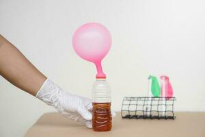 Hand holds pink inflated balloons on top of transparent test bottles with soft drink mix baking soda. Concept, science experiment about reaction of chemical substance. photo