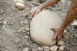 cerca arriba mano es levantamiento grande Roca desde suelo. concepto, pesado. difícil laboral. fuerte cuerpo a levantar o moverse pesado roca. foto