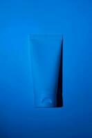 Plastic white tube on neon filter blue background. Skincare cleansing cosmetic. Beauty concept for face body care photo