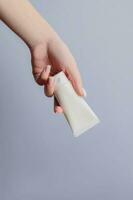 Woman's hand with a white plastic tube of cream on a gray background. Cosmetic products concept. Copy space. Mockup for design photo