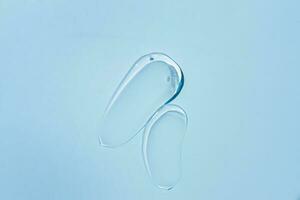 Squeezed cosmetic clear cream gel texture Iisolated on blue background. Close up transparent serum drop smear photo