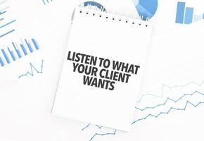 White notepad with text LISTEN TO WHAT YOUR CLIENT WANTS on the financial documentation. Finance and business concept photo