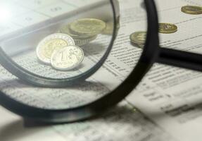 A magnifying glass with coins in the background isolated on an empty white background photo