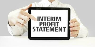 Text INTERIM PROFIT STATEMENT on tablet display in businessman hands on the white bakcground. Business concept photo