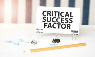 CRITICAL SUCCESS FACTOR sign on paper on white desk with office tools. Blue and white background photo