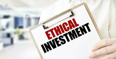 Text ETHICAL INVESTMENT on white paper plate in businessman hands in office. Business concept photo