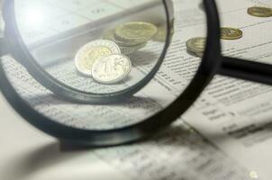 A magnifying glass with coins in the background isolated on an empty white background photo