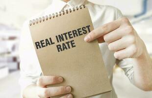 Text REAL INTEREST RATE on brown paper notepad in businessman hands in office. Business concept photo