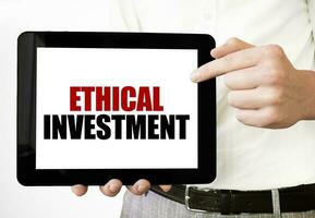 Text ETHICAL INVESTMENT on tablet display in businessman hands on the white background. Business concept photo