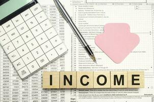 Wooden cubes with INCOME word with pen, calculator and pink arrow photo