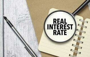 REAL INTEREST RATE words on magnifier glass with notebook and pen photo