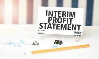 INTERIM PROFIT STATEMENT sign on paper on white desk with office tools. Blue and white background photo