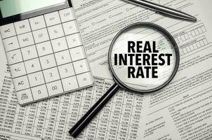REAL INTEREST RATE words on magnifier glass and calculator with pen photo