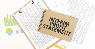 Text INTERIM PROFIT STATEMENT on brown paper notepad on the table with diagram. Business concept photo