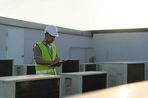 asiático mantenimiento ingeniero trabajos en el techo de fábrica. contratista inspeccionar compresor sistema y planes instalación de aire condición sistemas en construcción. Lista de Verificación, inspector, controlar foto