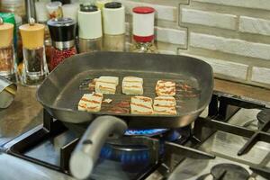 Halloumi cheese is fried on ribbed pan over fire on gas stove photo