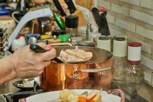 cocinero vierte pollo caldo desde cobre maceta dentro plato de pollo piernas foto