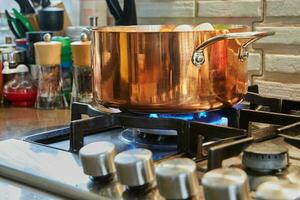 Copper saucepan with dish being prepared on fire on gas stove photo