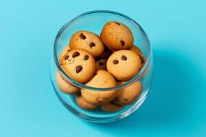 A glass bowl filled with chocolate chip cookies on a solid color background. photo