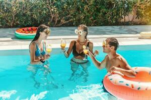 grupo de amigos en traje de baño bebida un cóctel en un nadando piscina foto