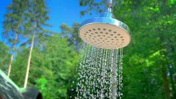 Jets of water pour from the shower against the background of green vegetation on a hot day. video