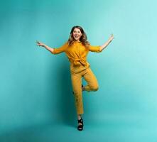 Brunette girl with a yellow clothes jumps over a cyan background. Concept of fashion and shopping with joyful expression photo
