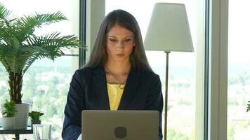 a woman in glasses is looking at her laptop working inside modern office video