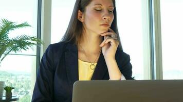 un mujer en lentes es mirando a su ordenador portátil trabajando dentro moderno oficina video