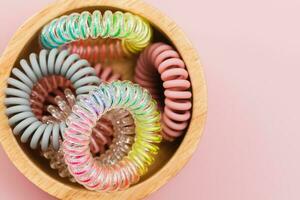 The wooden bowl of spiral hair rubber bands on pink background photo