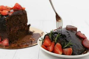 A stainless fork scooping a piece of delicious chocolate cake with strawberries photo