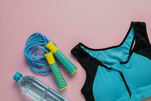 Sport bra for exercise, fresh drinking water and jump rope on pink background photo