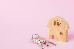 Wooden house model with keys on soft pink background photo