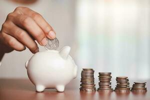Hand saving a coin into piggy bank with step of coins and money on the wooden table photo