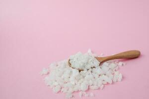 Sea salt in a wooden spoon on pink background photo